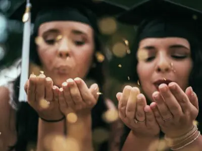 two graduates blowing glitter from their hands