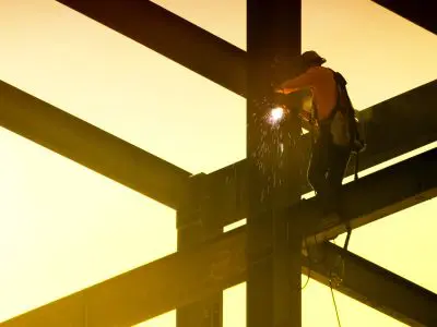 A construction worker sitting atop a steel beam well above the ground, working on a building.