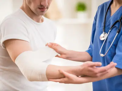 A female physician treating a male patient's arm injury by dressing it.
