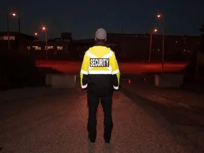 A man with a bright yellow security jacket standing in front of a building.