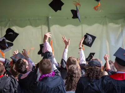 A group of students celebrating at a graduation ceremony by tossing their caps and tassels into the air.