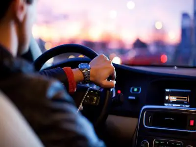 A man's left hand guiding the steering wheel of a car.