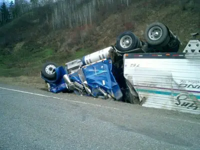 Big rig truck upside down on the side of the road.