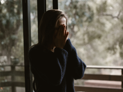 woman standing with her hands in her face by a window. Mental health angle.