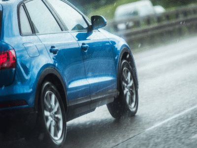 A blue sedan on the freeway while its raining.
