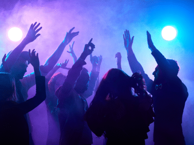 Dark figures dancing with their hands up with colorful lights.