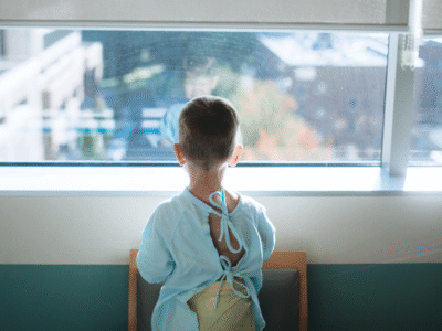 A young boy in a hospital gown looking out the window.