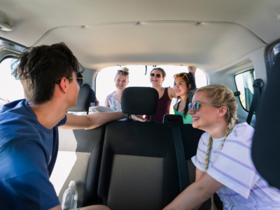 Group of young people sitting inside a van, smiling and talking, suggesting a church or youth group outing where transportation safety and liability waivers may be relevant.