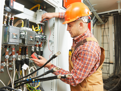 An electrician wearing protective gear inspects and tests a live electrical panel on a construction site, highlighting the complex and dangerous conditions where expert analysis is often needed to prove fault in electrocution injury cases.
