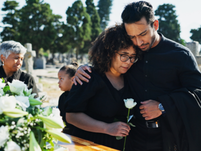 Grieving family gathered beside a casket with white flowers during a funeral, illustrating the emotional and financial losses involved in a wrongful death claim.