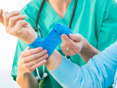 Healthcare professional wrapping a patient's burned wrist with a blue bandage, representing treatment and ongoing medical care for a severe burn injury.