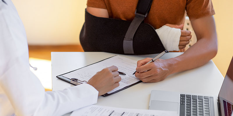 person with arm in a sling signing medical forms with a doctor