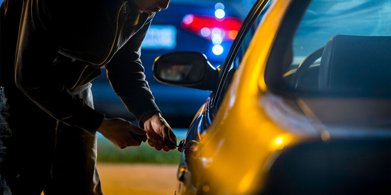 person in dark clothing picking the lock of a car in a dark parking lot
